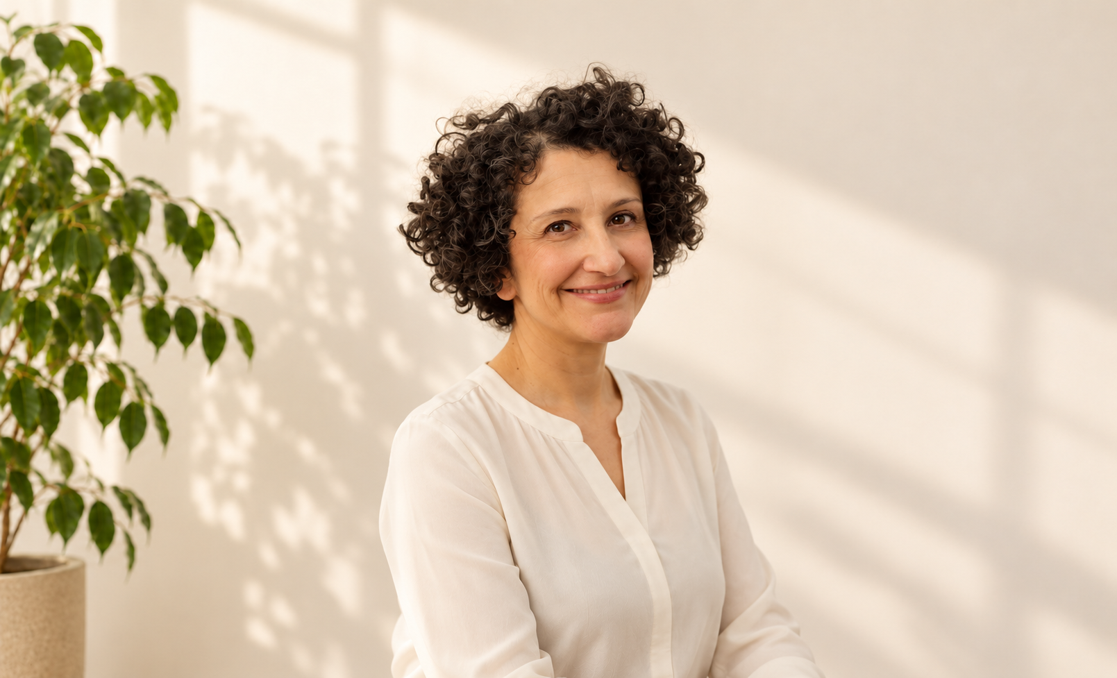 Elena sorridente in una stanza luminosa con parete crema e Ficus benjamina